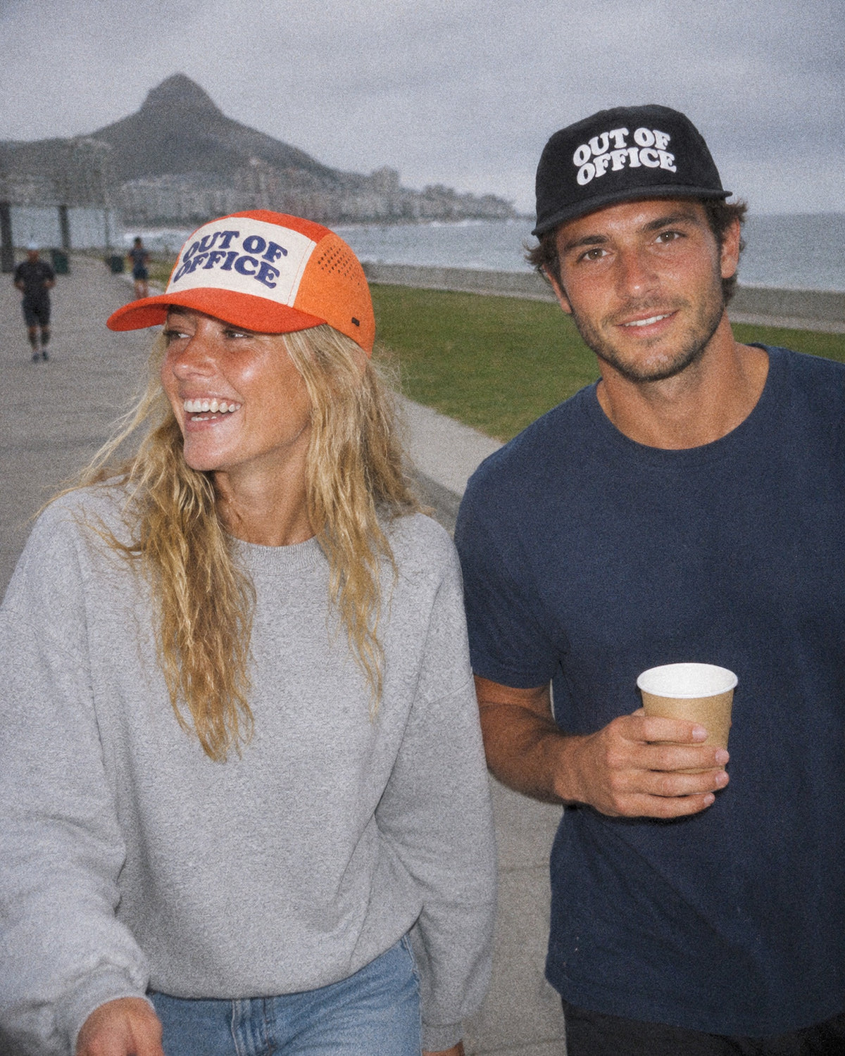 Two friends on the Sea Point promenade in orange and black Out of Office caps