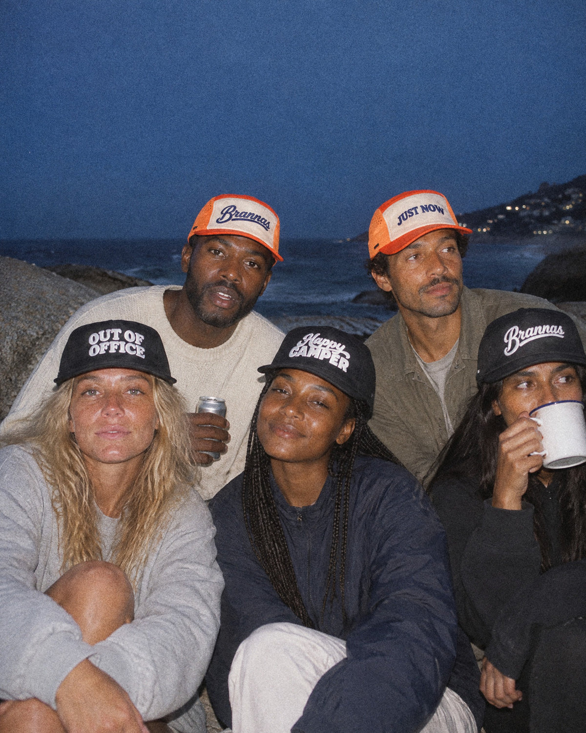 Five friends on the Camps Bay boulders at dusk wearing Sundowners Club caps